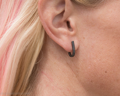 Hand hammered oxidized black sterling silver J-Curve hoop earrings, oxidized black patina, worn on ear.
