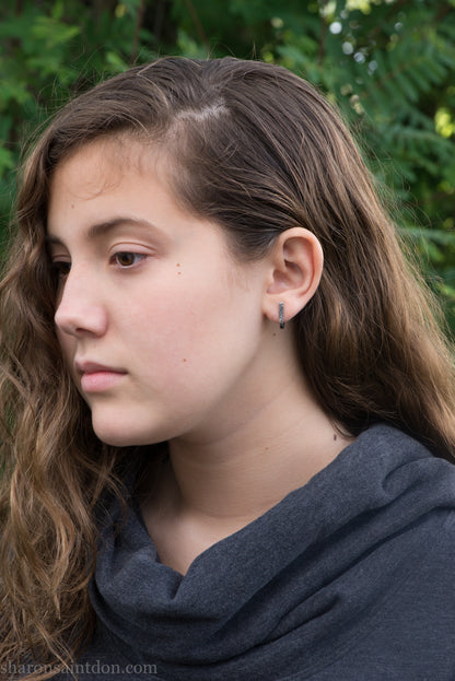 Hand hammered oxidized sterling silver J-wrap hoop earring, dark antique patina, worn on ear.
