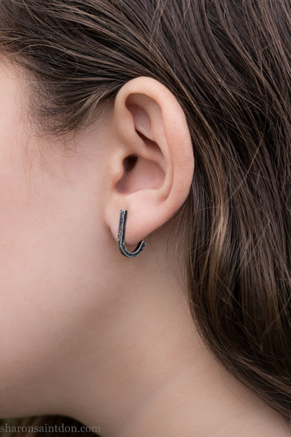 Hand hammered oxidized sterling silver J-wrap hoop earring, dark antique patina, worn on ear.