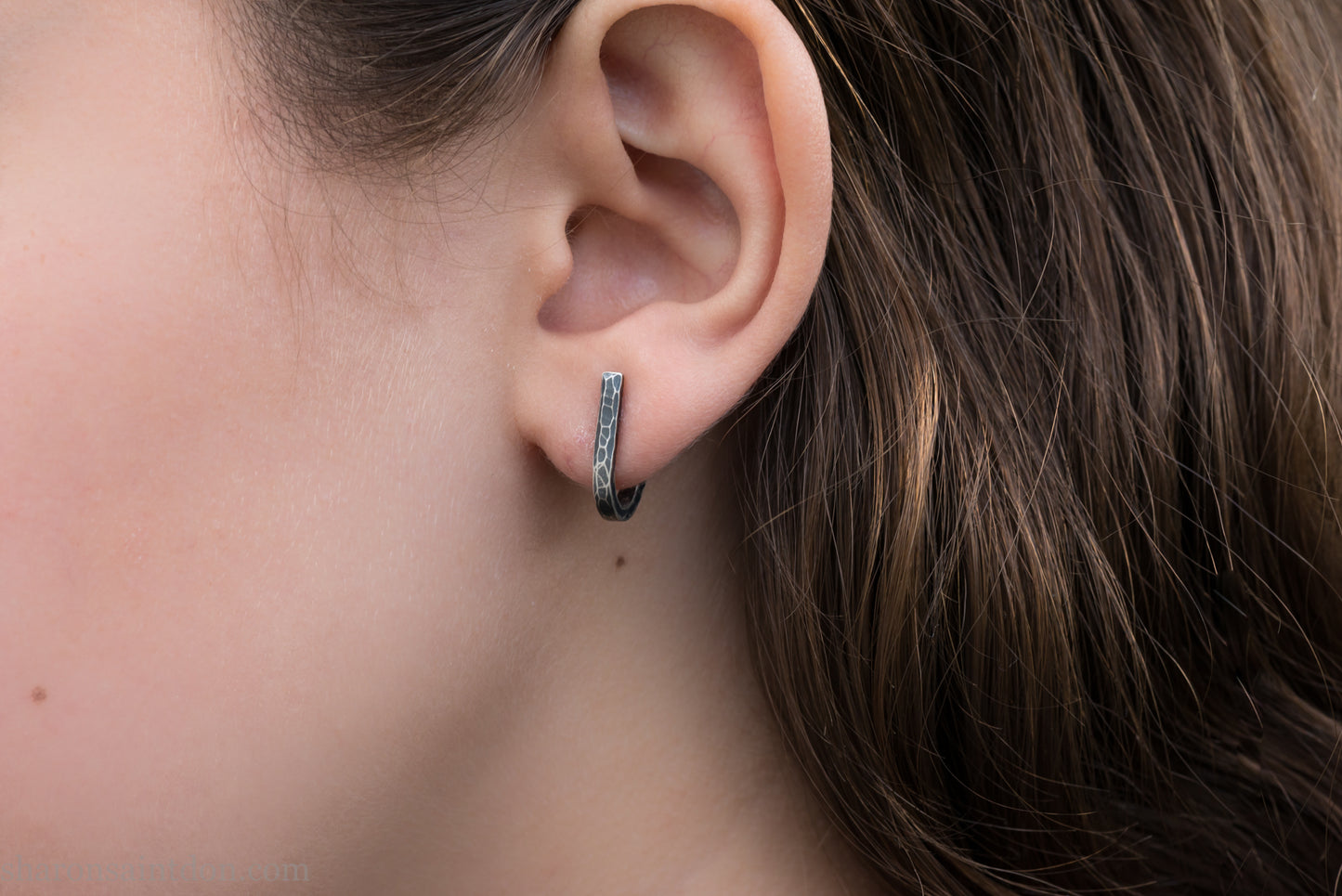 Hand hammered oxidized sterling silver J-wrap hoop earring, dark antique patina, worn on ear.