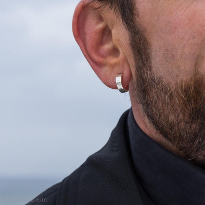 Close up photo of a man wearing handcrafted 14mm x 4mm hammered solid sterling silver hoop earrings.