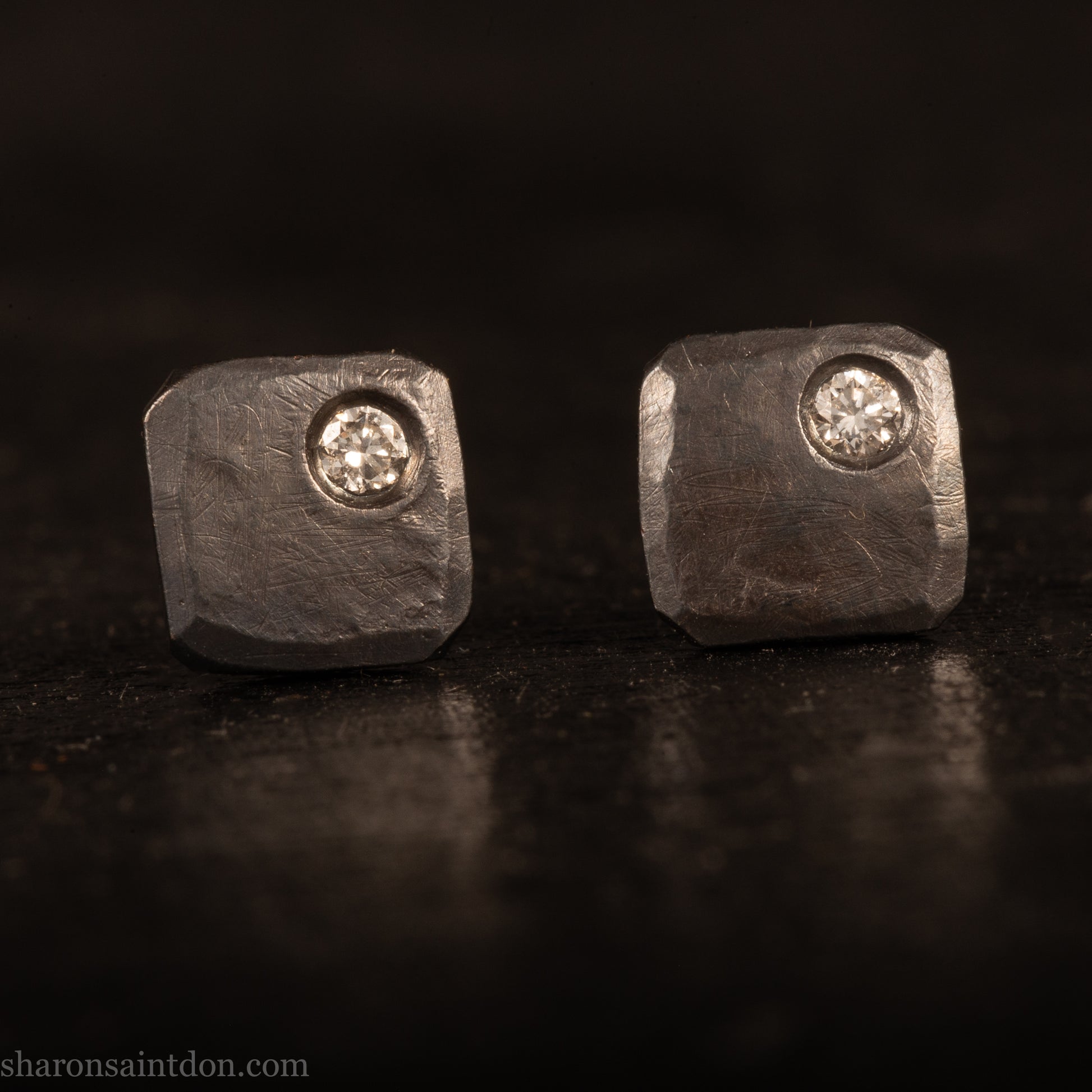 Handcrafted 925 sterling silver stud earrings with moissanite, lab grown, alternative diamond gemstones. 7mm square, 1.5mm thick, solid hammered silver with oxidized black finish. 2mm round moissanite is set in the corner, posts and backs are sterling silver.