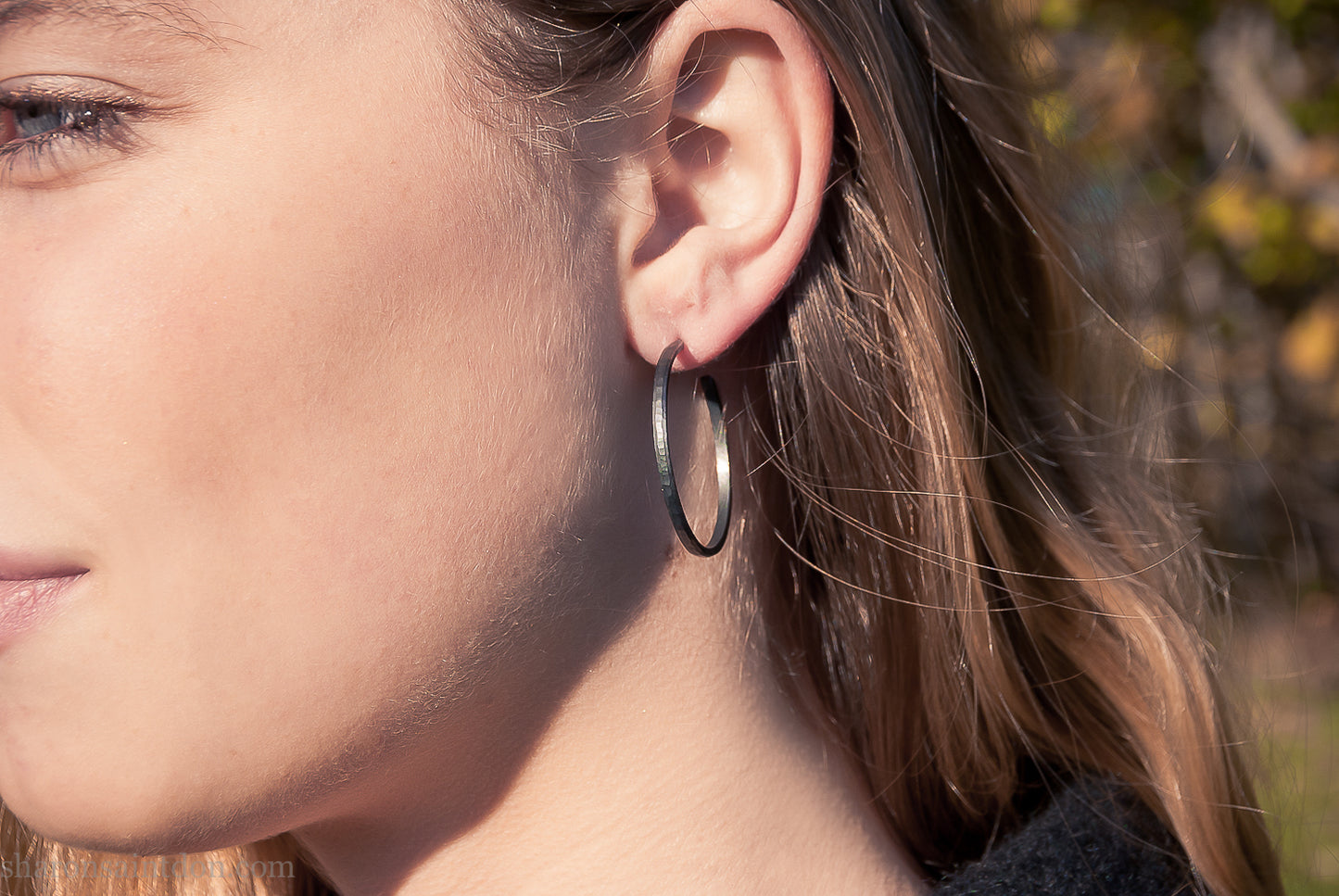 25mm oxidized black sterling silver round hammered hoop earring, close-up on model’s ear.