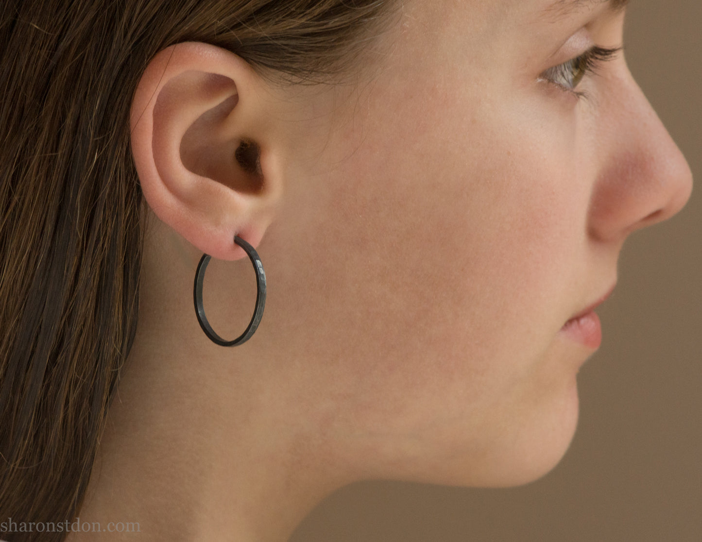 25mm oxidized black sterling silver round hammered hoop earring, close-up on model’s ear.