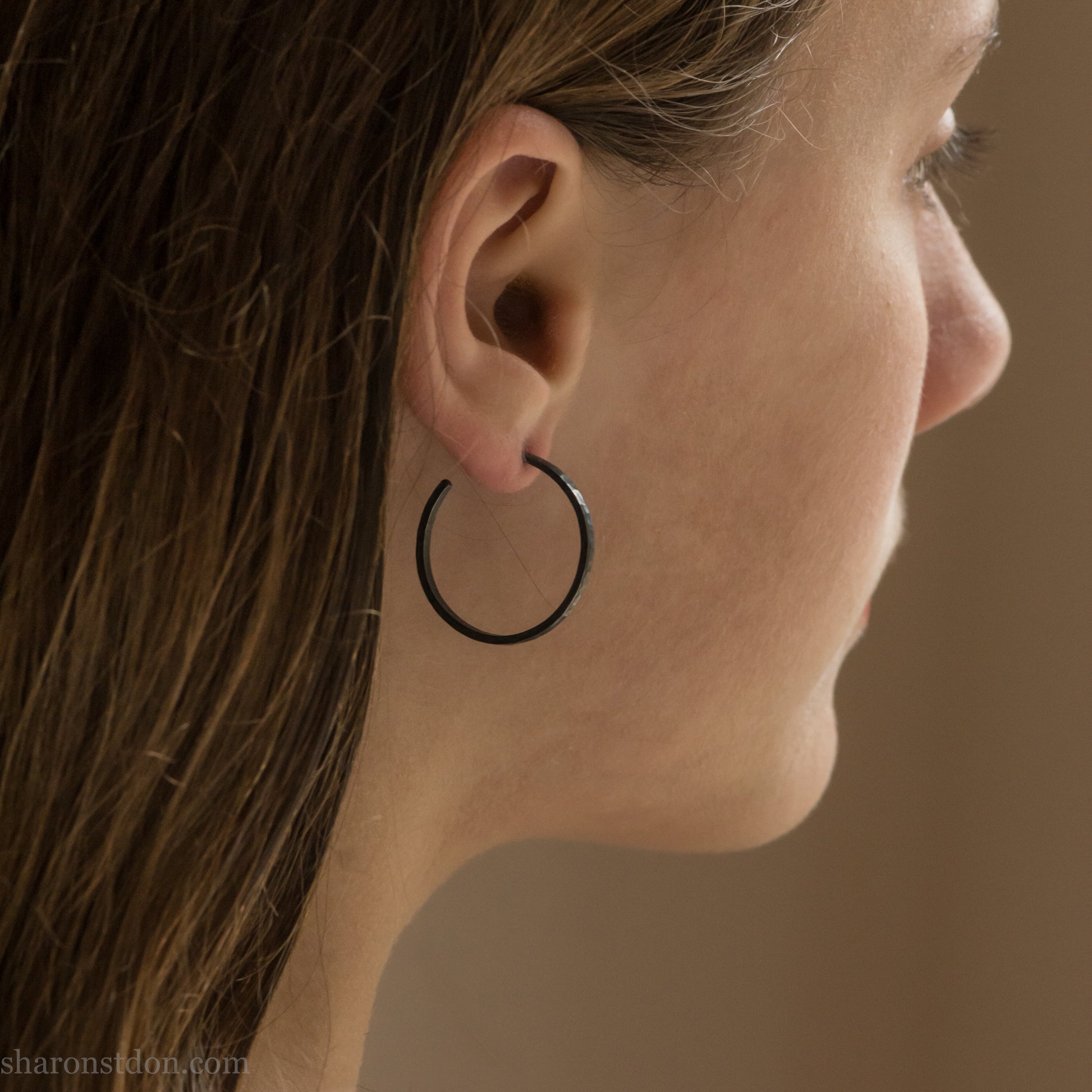 25mm oxidized black sterling silver round hammered hoop earring, close-up on model’s ear.