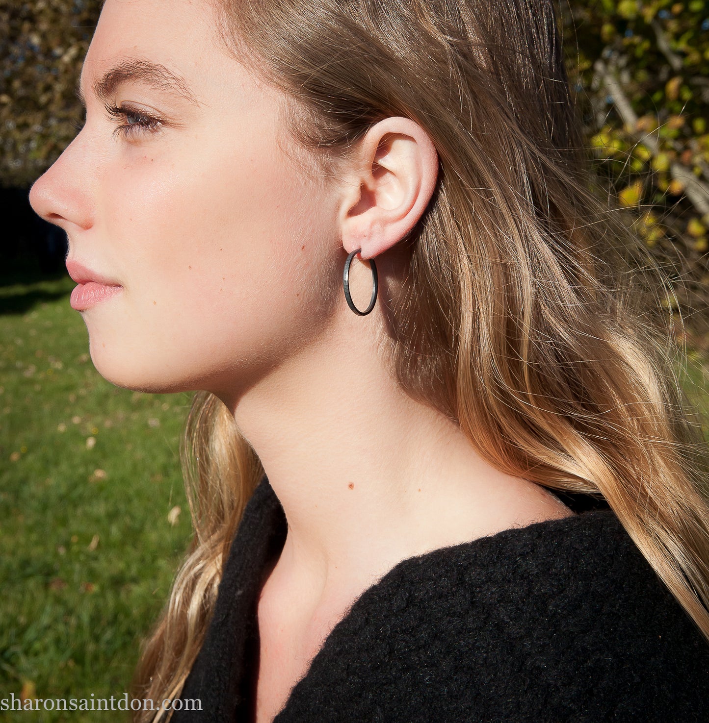 25mm oxidized black sterling silver round hammered hoop earring, close-up on model’s ear.