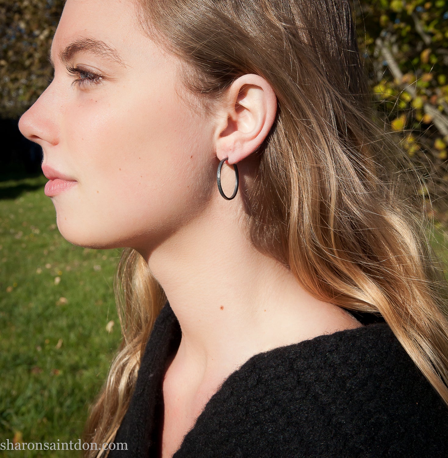 25mm oxidized black sterling silver round hammered hoop earring, close-up on model’s ear.