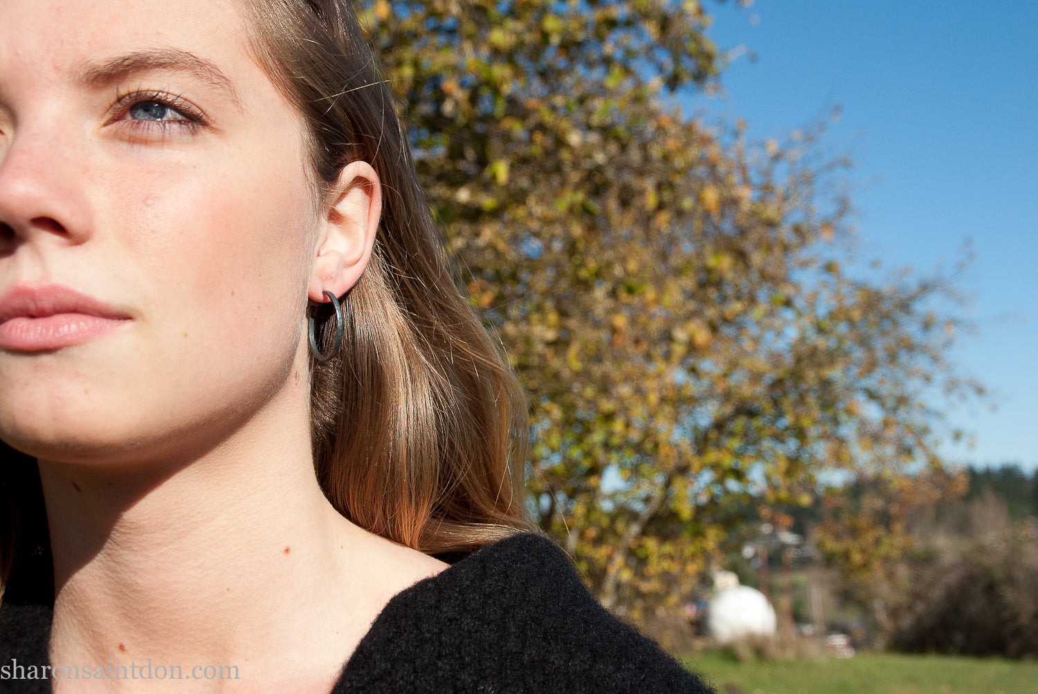 25mm oxidized black sterling silver round hammered hoop earring, close-up on model’s ear.
