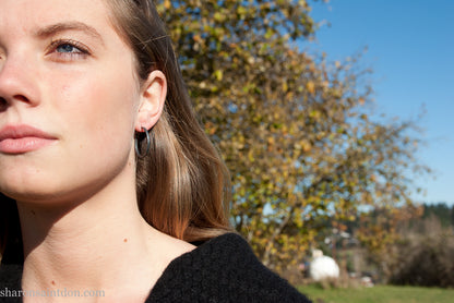 25mm oxidized black sterling silver round hammered hoop earring, close-up on model’s ear.