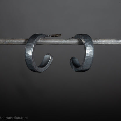 Close up photo of oxidized black, handcrafted 14mm x 3mm hammered solid sterling silver hoop earrings.