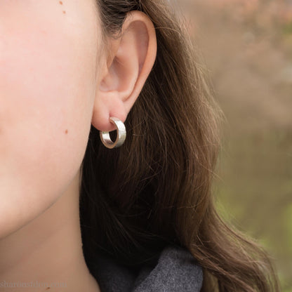 Close up photo of a person wearing a handcrafted 14mm x 4mm hammered solid sterling silver hoop earring.