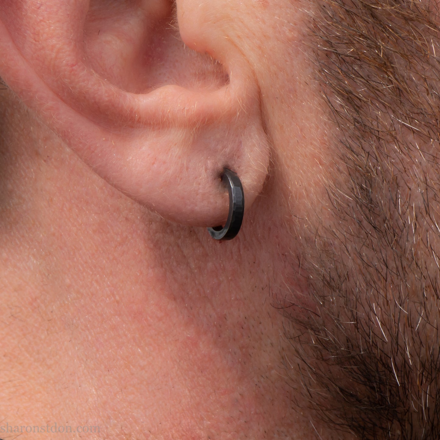 Solid 925 sterling silver hoop earrings for men with an oxidized matte black finish. 12mm exterior diameter, 9mm interior, 2mm wide, and 1.5mm thick. Solid sterling silver posts and backs. Handcrafted, each pair hand hammered by Sharon Saint Don in the Pacific Northwest of the USA. Worn by a man with light skin, dark hair and beard.