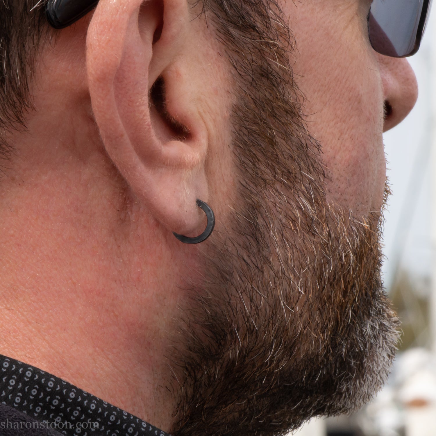 Solid 925 sterling silver hoop earrings for men with an oxidized matte black finish. 12mm exterior diameter, 9mm interior, 2mm wide, and 1.5mm thick. Solid sterling silver posts and backs. Handcrafted, each pair hand hammered by Sharon Saint Don in the Pacific Northwest of the USA. Worn by a man with light skin, dark hair and beard.