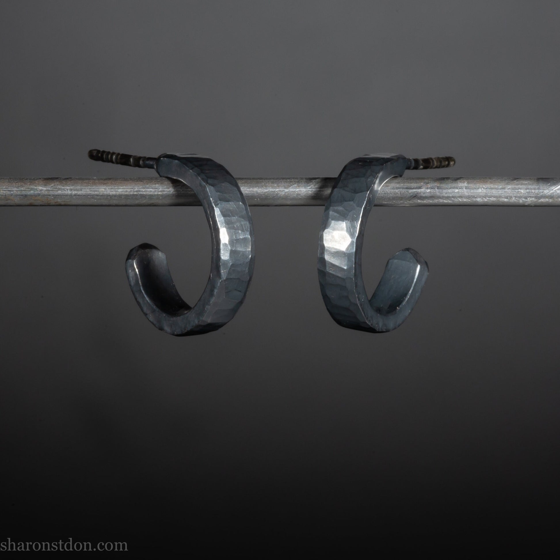 Close up photo of oxidized black, handcrafted 14mm x 3mm hammered solid sterling silver hoop earrings.