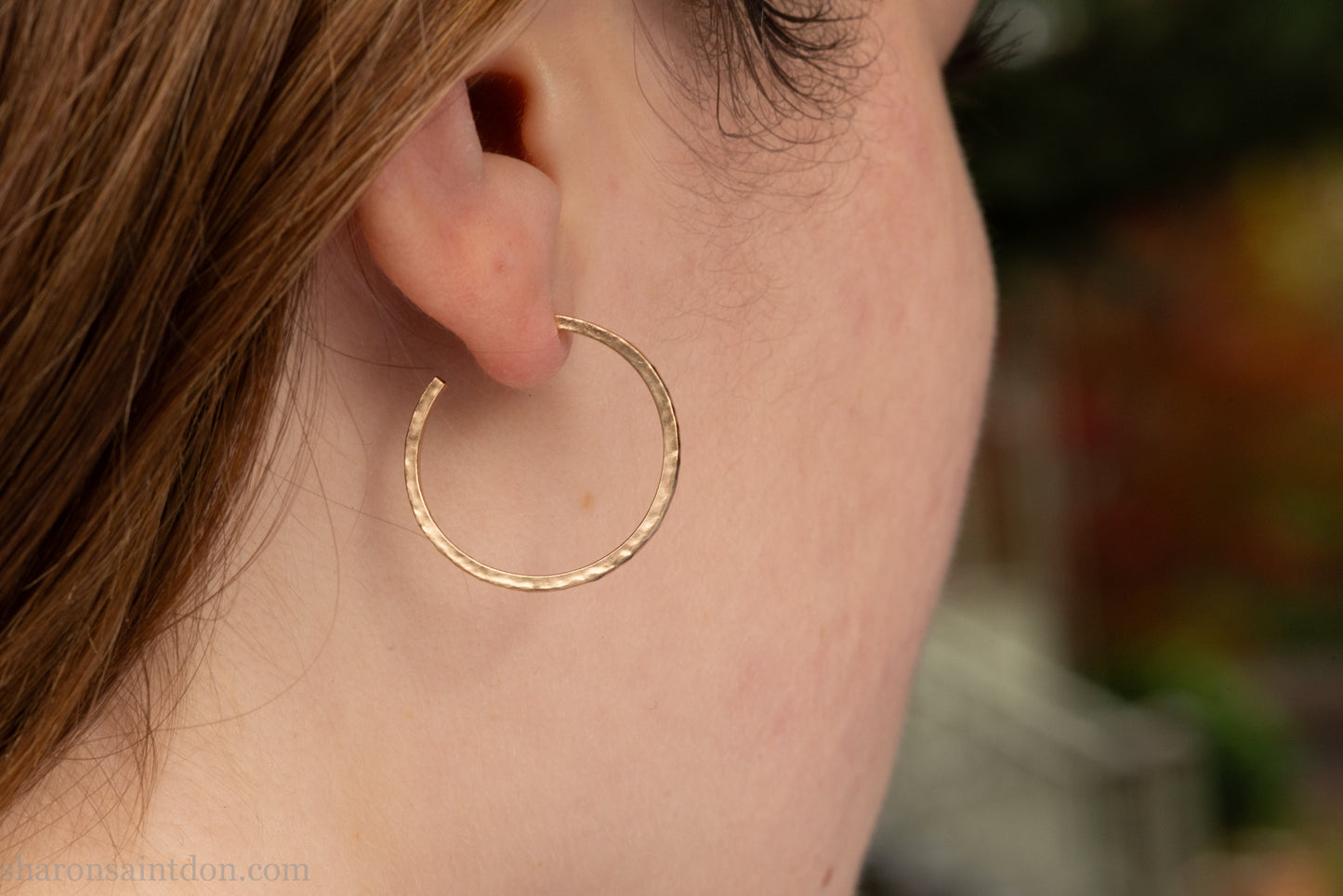 Solid hammered yellow gold hoop earrings with brushed, matte finish, gold posts and  locking backs; worn on ear.