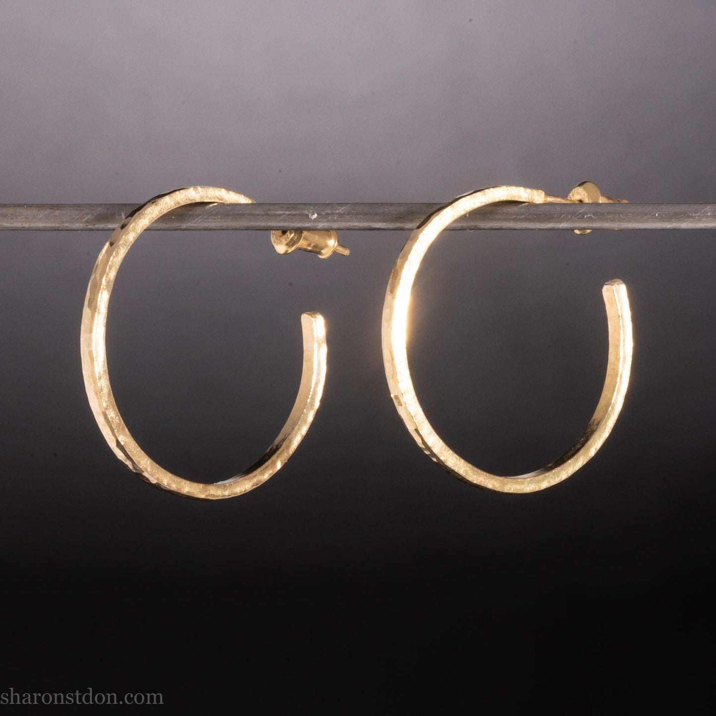 Solid 14k gold hoop earrings handmade in North America by Sharon SaintDon. Solid hammered yellow gold with a matte brushed finish. 25mm diameter round, 1.5mm thick, solid gold posts and backs.