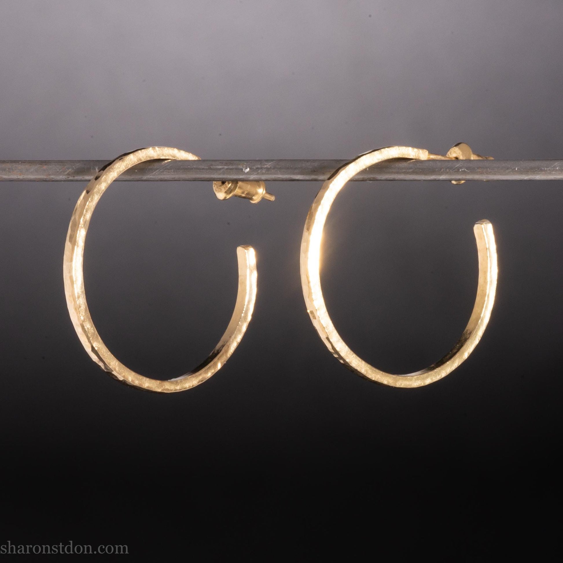 Solid 14k gold hoop earrings handmade in North America by Sharon SaintDon. Solid hammered yellow gold with a matte brushed finish. 25mm diameter round, 1.5mm thick, solid gold posts and backs.