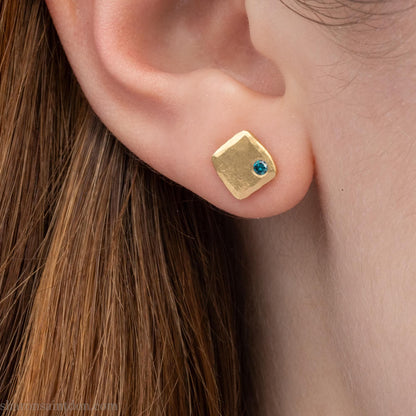 Solid yellow gold square stud earrings with 2mm blue diamonds, matte finish, shown worn on a model (side view, one ear).