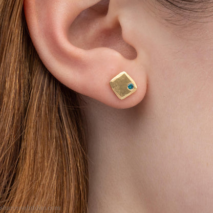 Solid yellow gold square stud earrings with 2mm blue diamonds, matte finish, shown worn on a model (side view, one ear).