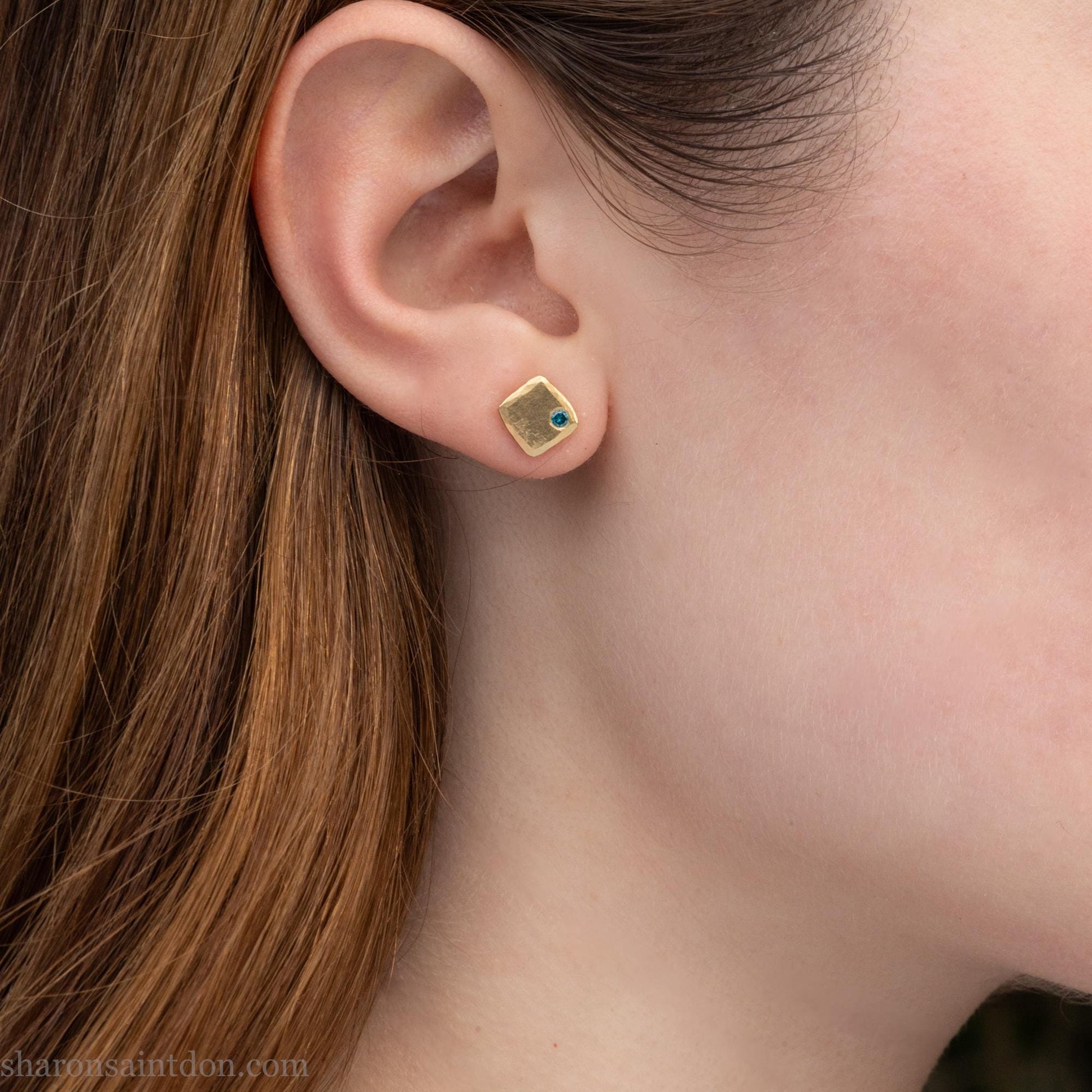 Solid yellow gold square stud earrings with 2mm blue diamonds, matte finish, shown worn on a model (side view, one ear).