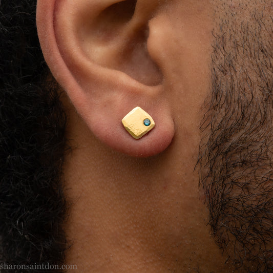 Solid yellow gold square stud earrings with 2mm blue diamonds, matte finish, shown worn on a model with a beard (side view, one ear).
