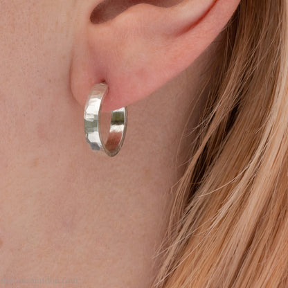 Close-up view of a person wearing hand-hammered 925 sterling silver hoop earring, 14mm diameter, 3mm wide, 1.5mm thick, brushed matte satin finish.