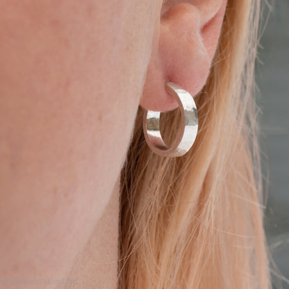 Close-up view of a person wearing hand-hammered 925 sterling silver hoop earring, 14mm diameter, 3mm wide, 1.5mm thick, brushed matte satin finish.