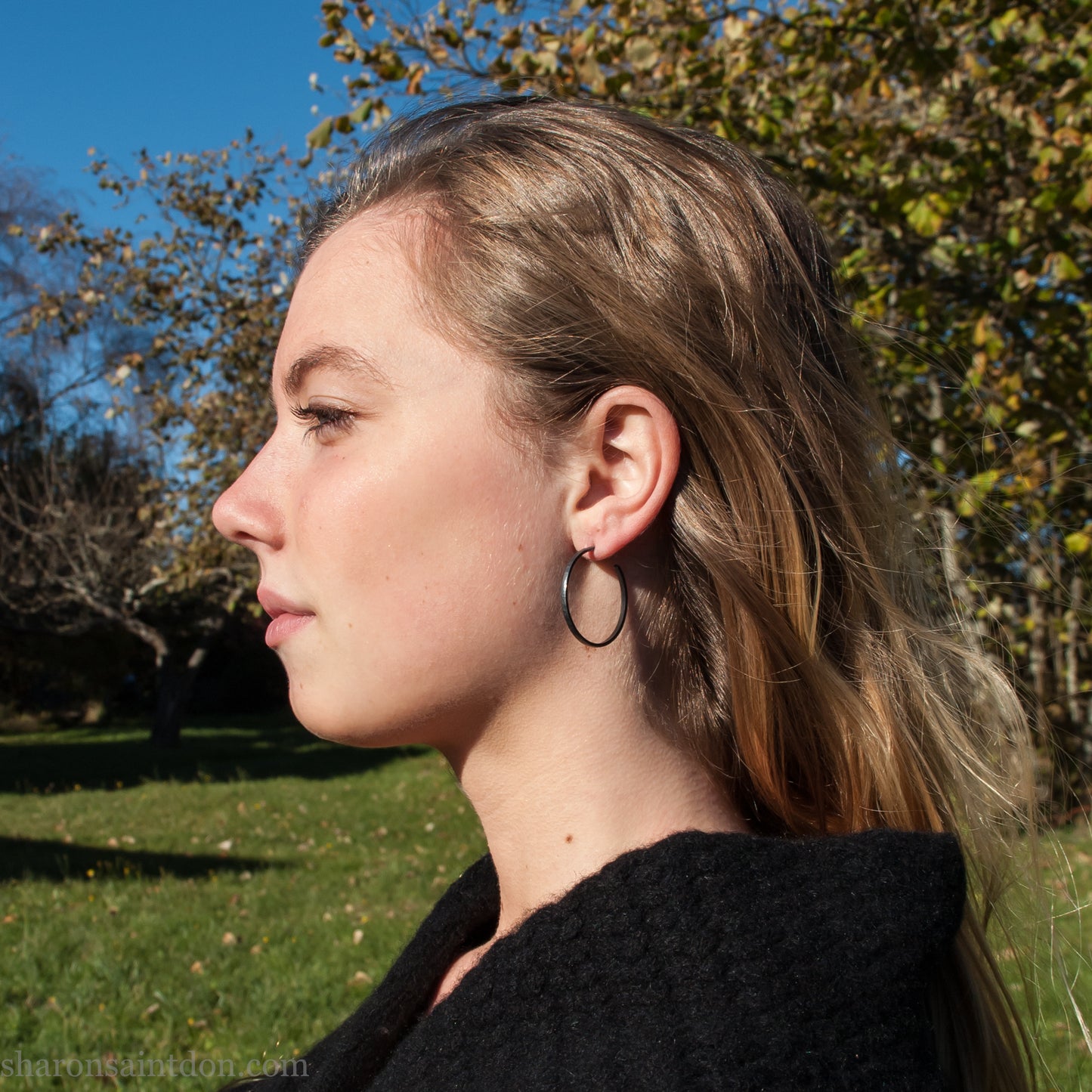 Oxidized black sterling silver hammered round hoop earring, shown worn on a model’s ear. 30mm diameter, 2mm wide, solid hammered silver.