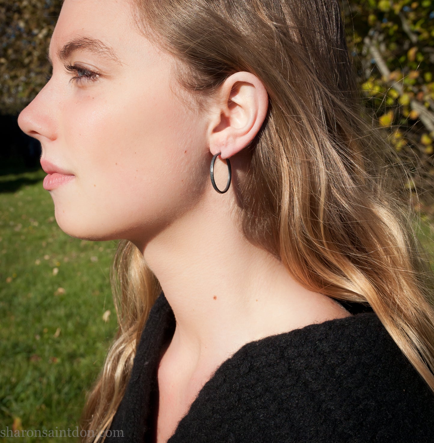 Oxidized black sterling silver hammered round hoop earring, shown worn on a model’s ear. 30mm diameter, 2mm wide, solid hammered silver.