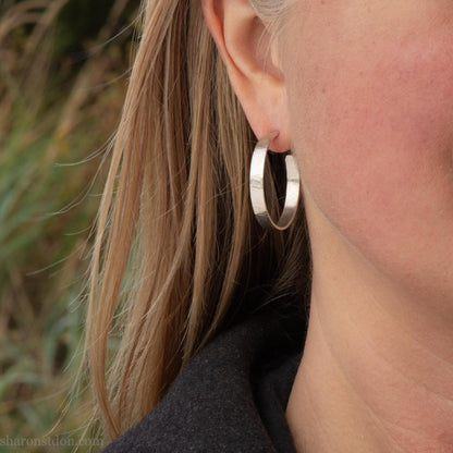 30 mm x 4 mm solid sterling silver hoop earrings, handmade with wavy hammered texture and shiny matte finish, shown on a model with long blonde hair.