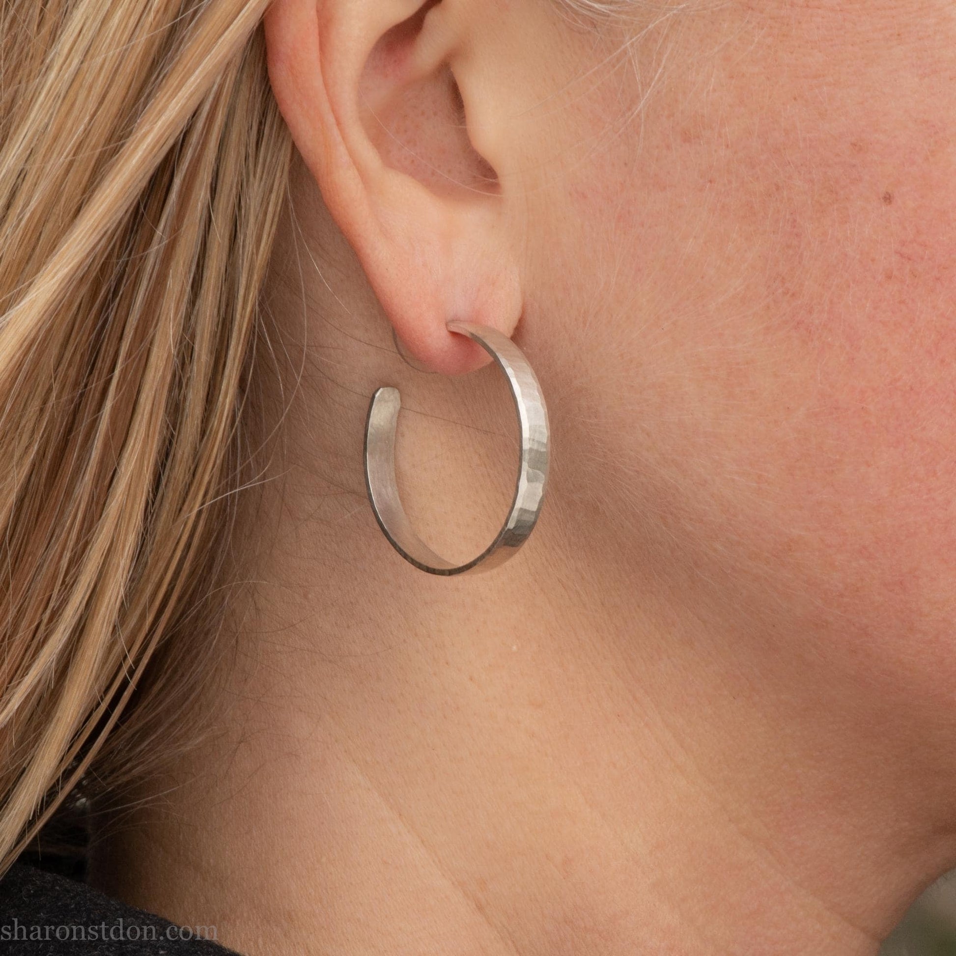 30 mm x 4 mm solid sterling silver hoop earrings, handmade with wavy hammered texture and shiny matte finish, shown on a model with long blonde hair.