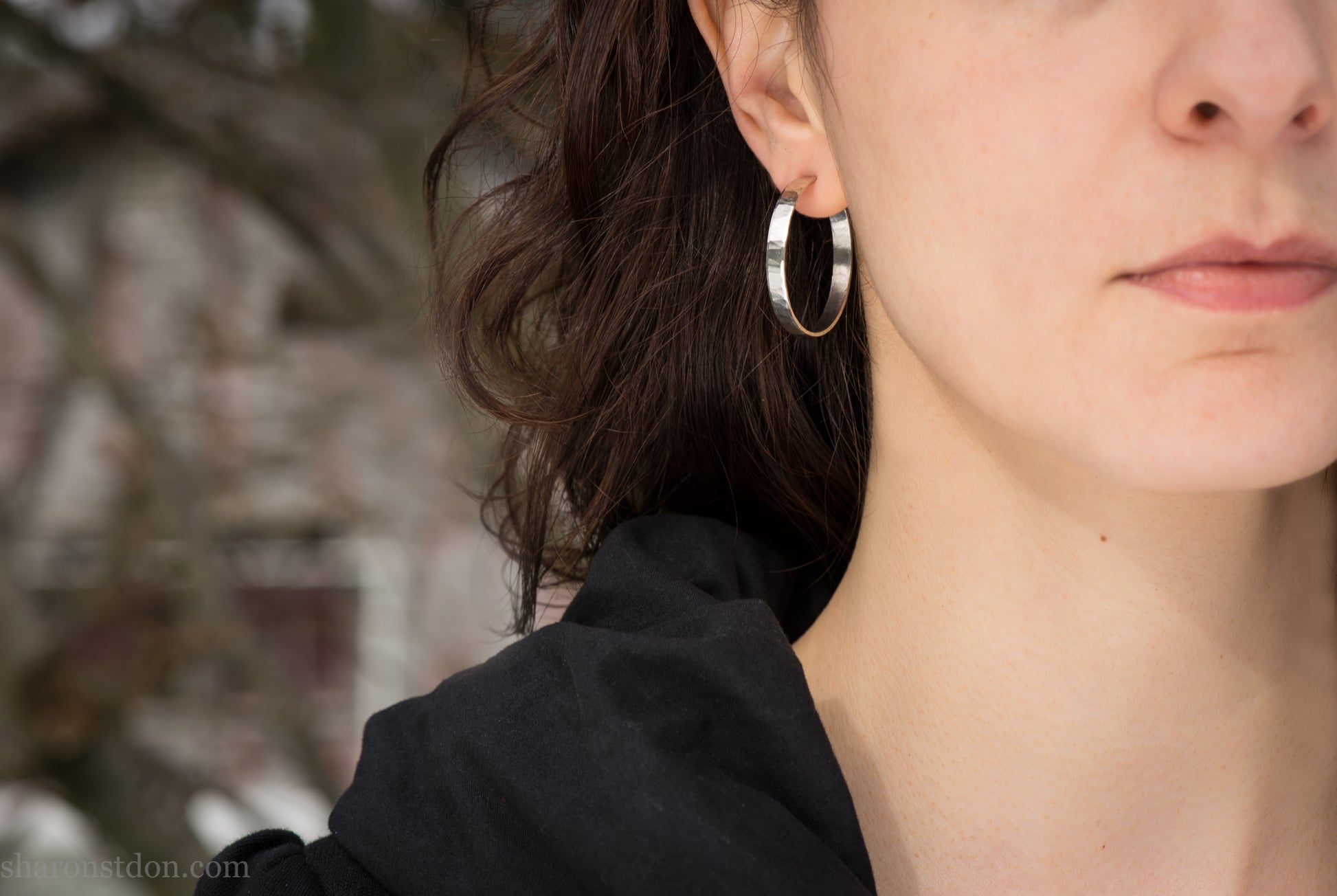 30 mm x 4 mm solid sterling silver hoop earrings, handmade with wavy hammered texture and shiny matte finish, shown on a model with long brown hair.