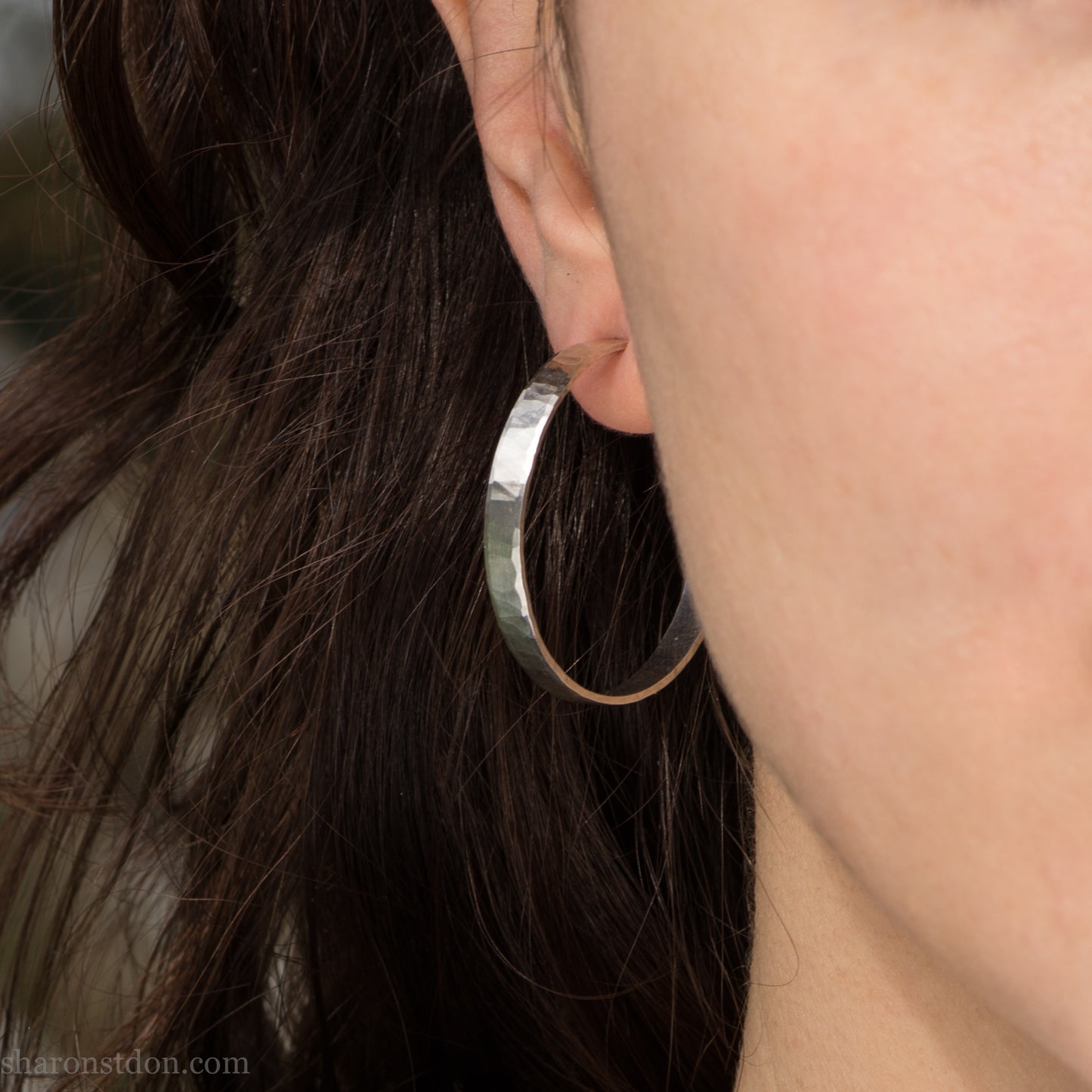 30 mm x 4 mm solid sterling silver hoop earrings, handmade with wavy hammered texture and shiny matte finish, shown on a model with long brown hair.