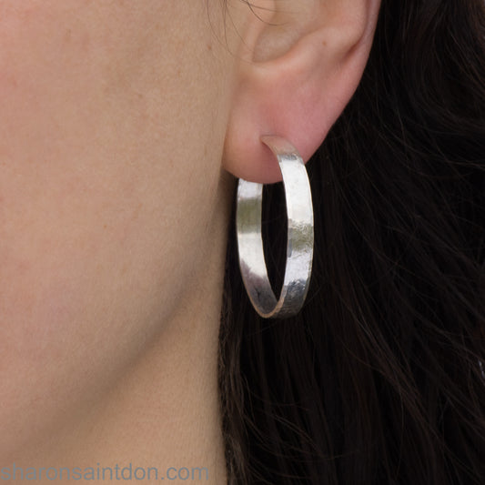 30mm hand-hammered sterling silver hoop earring with a matte satin finish, shown worn on an ear.