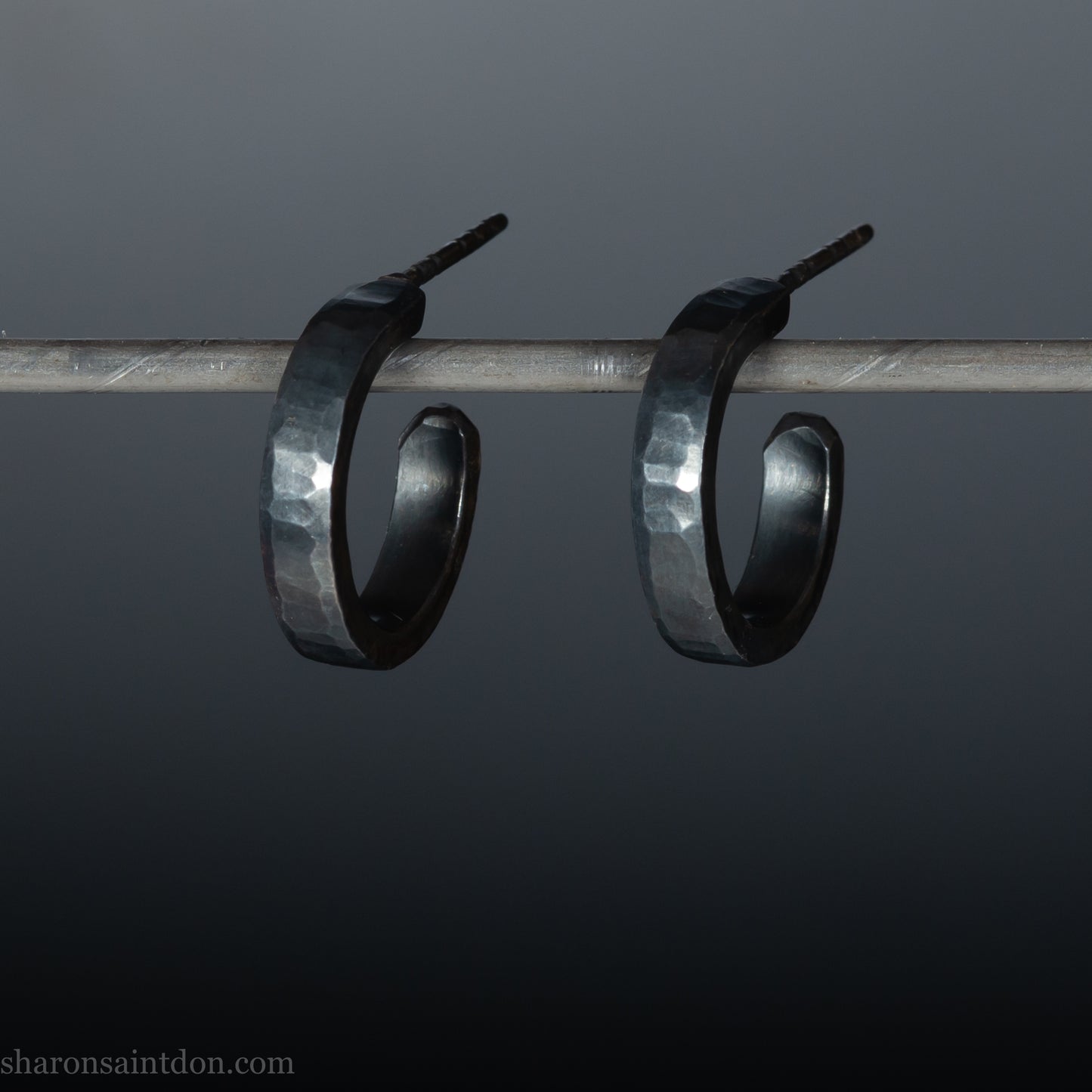 Solid 925 sterling silver hoop earrings with an oxidized, matte, black finish. 18mm exterior diameter, 15mm interior, 3mm wide, and 1.5mm thick. Solid sterling silver posts and backs. Handcrafted in the USA, each pair hand hammered by Sharon Saint Don.