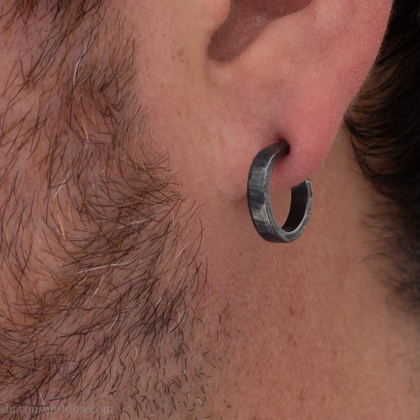 Solid 925 sterling silver hoop earrings for men with a shiny, matte finish. 18mm Solid 925 sterling silver hoop earrings with an oxidized, matte, black finish. 18mm exterior diameter, 15mm interior, 3mm wide, and 1.5mm thick. Solid sterling silver posts and backs. Handcrafted in the USA, each pair hand hammered by Sharon Saint Don. Worn by a man with light skin, dark hair and beard.