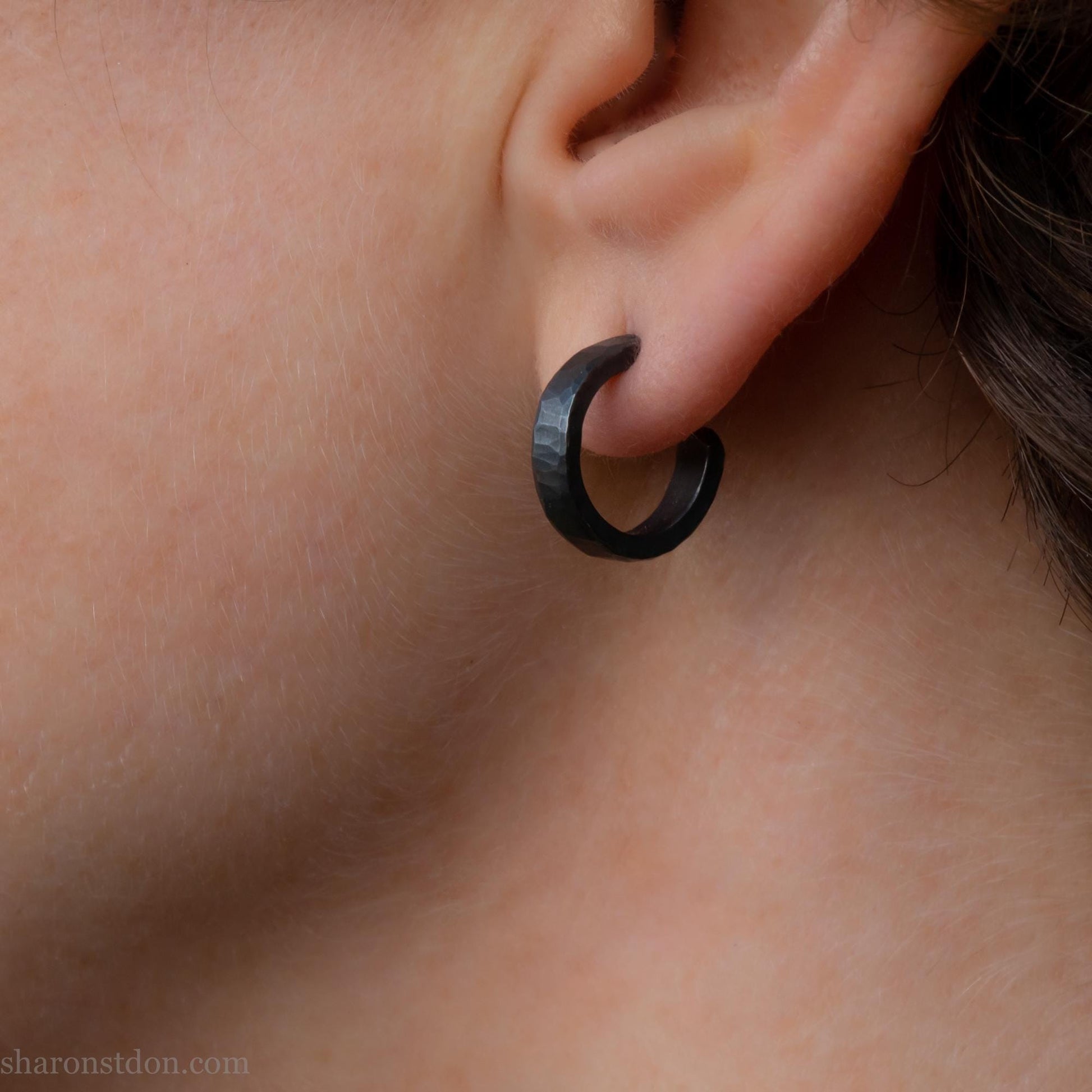 Close up photo of a person wearing oxidized black, handcrafted 14mm x 3mm hammered solid sterling silver hoop earrings.
