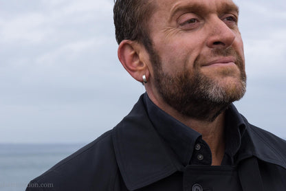 Close up photo of a man wearing handcrafted 14mm x 4mm hammered solid sterling silver hoop earrings.