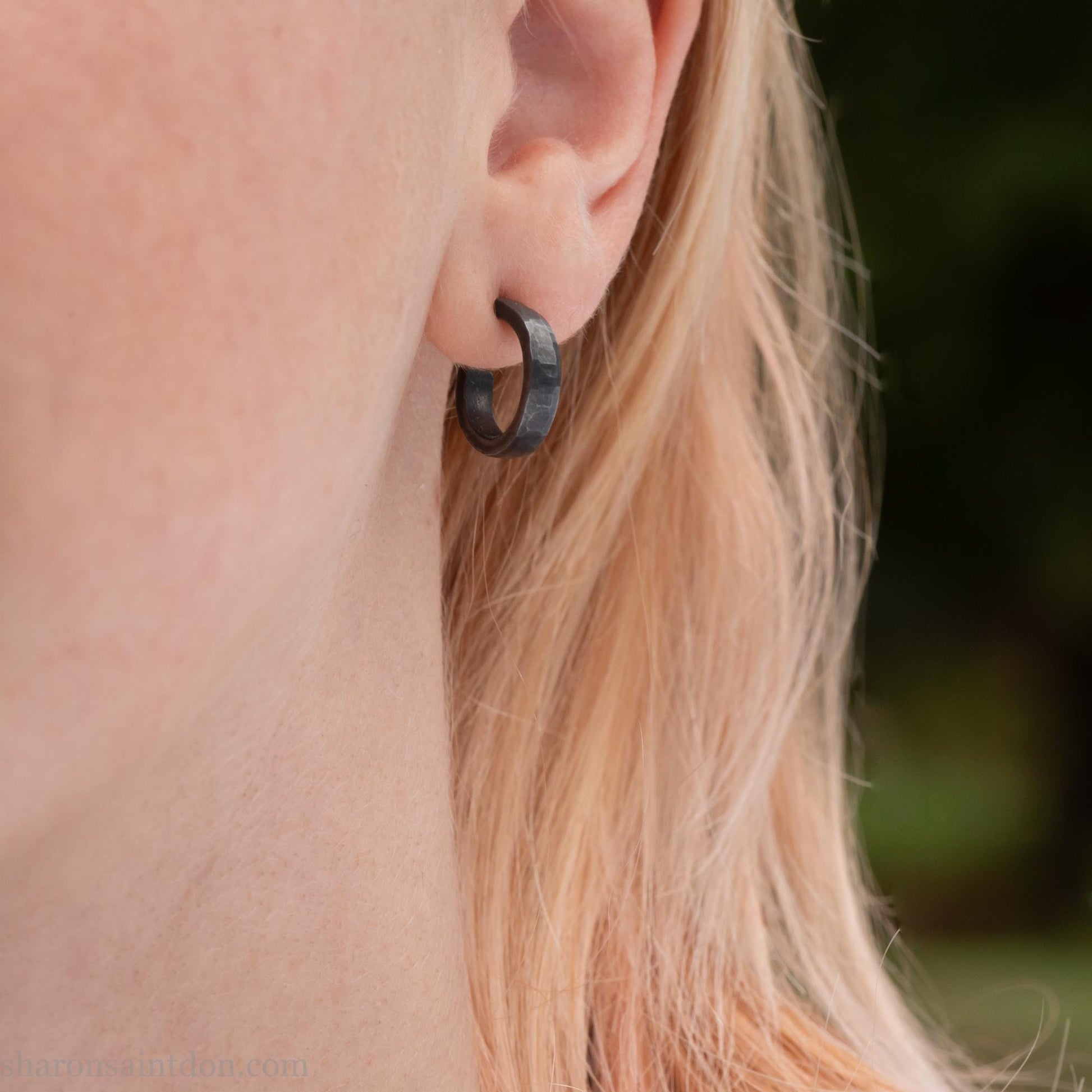 Close up photo of a person wearing oxidized black, handcrafted 14mm x 3mm hammered solid sterling silver hoop earrings.