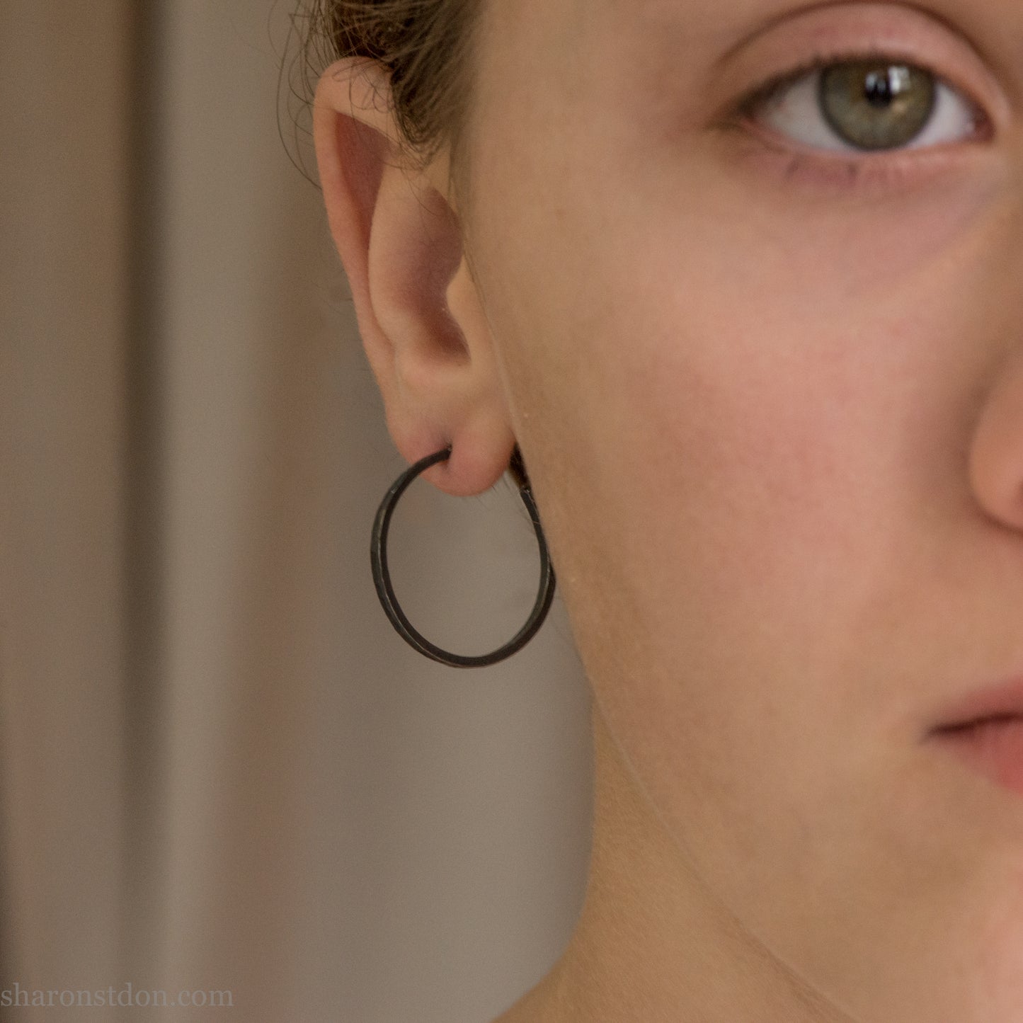 25mm oxidized black sterling silver round hammered hoop earring, close-up on model’s ear.