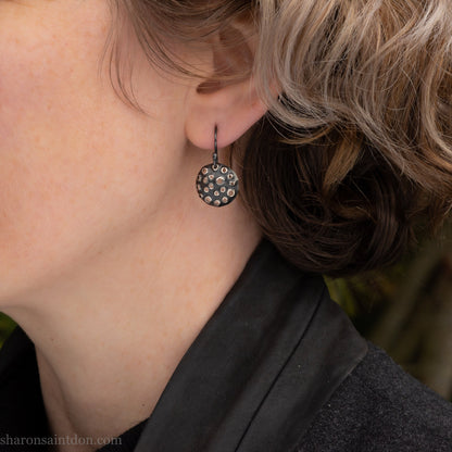 15mm solid 925 sterling silver round disc earrings, hand-punched pattern, dark antique patina, french hooks, worn on an ear.