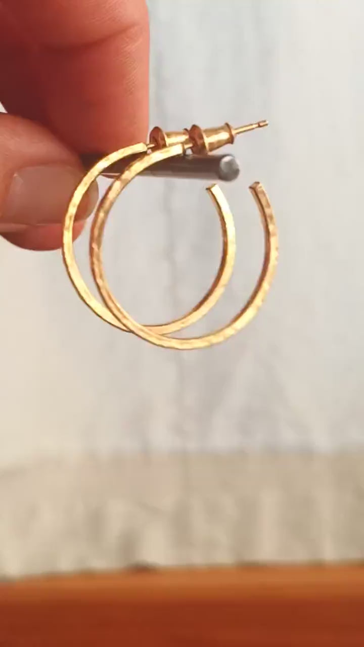 25mm diameter by 1.5mm thick handmade solid 14k yellow gold hoop earrings with solid 14k gold posts and backs. Handmade by Sharon SaintDon in North America. Hammered from solid gold with a matte finish.