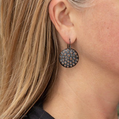 25mm solid 925 sterling silver round disc earrings worn on ear, hand-punched pattern, flat matte black oxidized finish