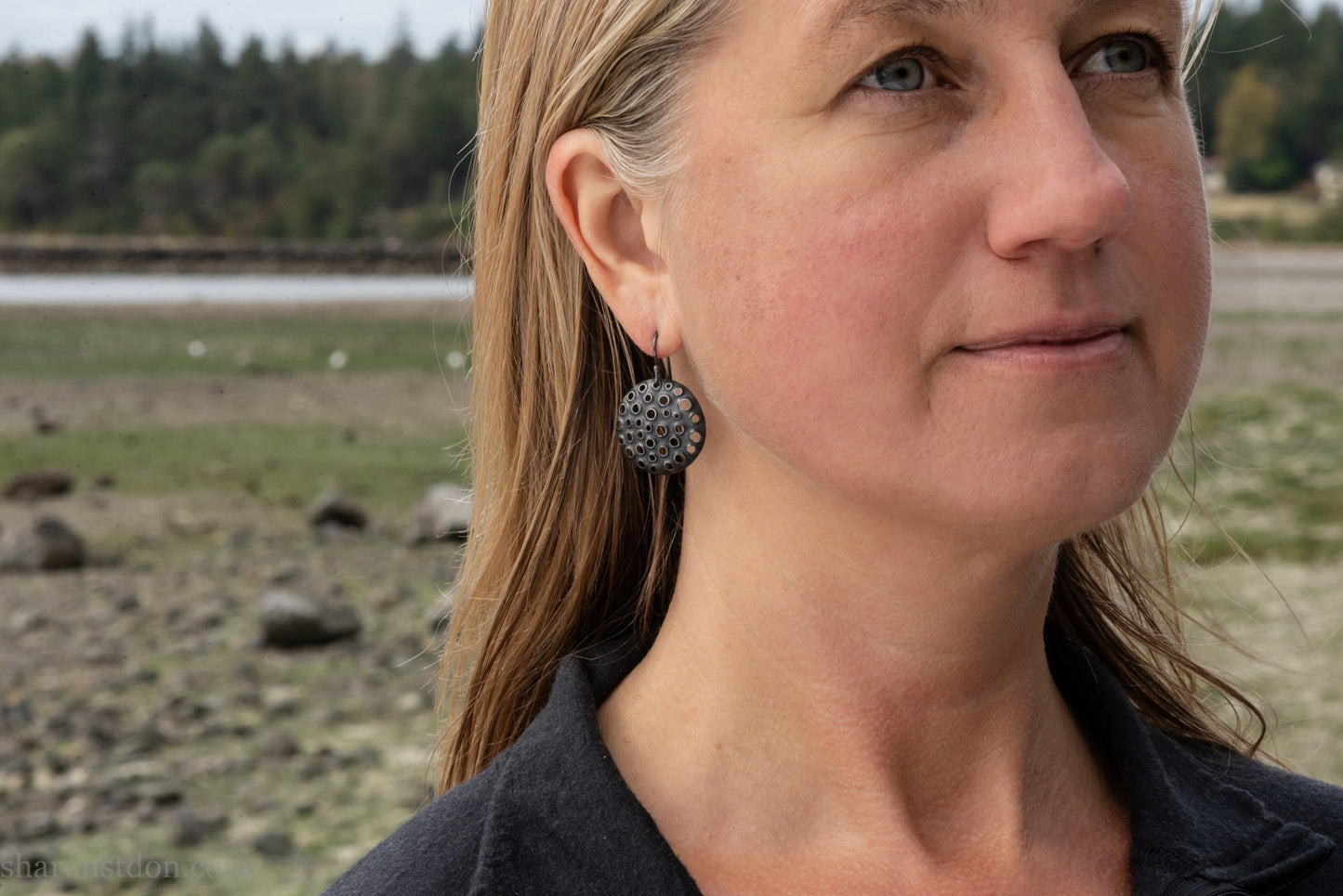 25mm solid 925 sterling silver round disc earrings worn on ear, hand-punched pattern, flat matte black oxidized finish.