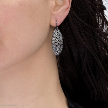 38mm solid 925 sterling silver oval disc earrings worn on ear, hand-punched pattern, dark antique patina with silver highlights.