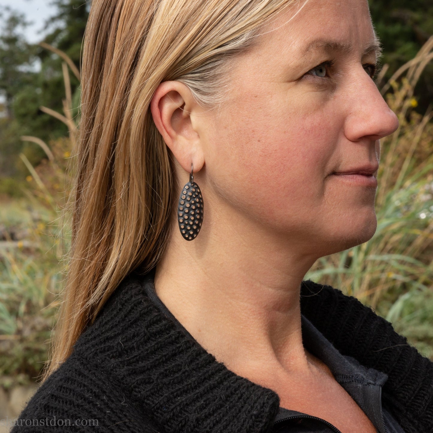 38mm solid 925 sterling silver oval disc earrings worn on ear, hand-punched pattern, flat matte black oxidized finish.