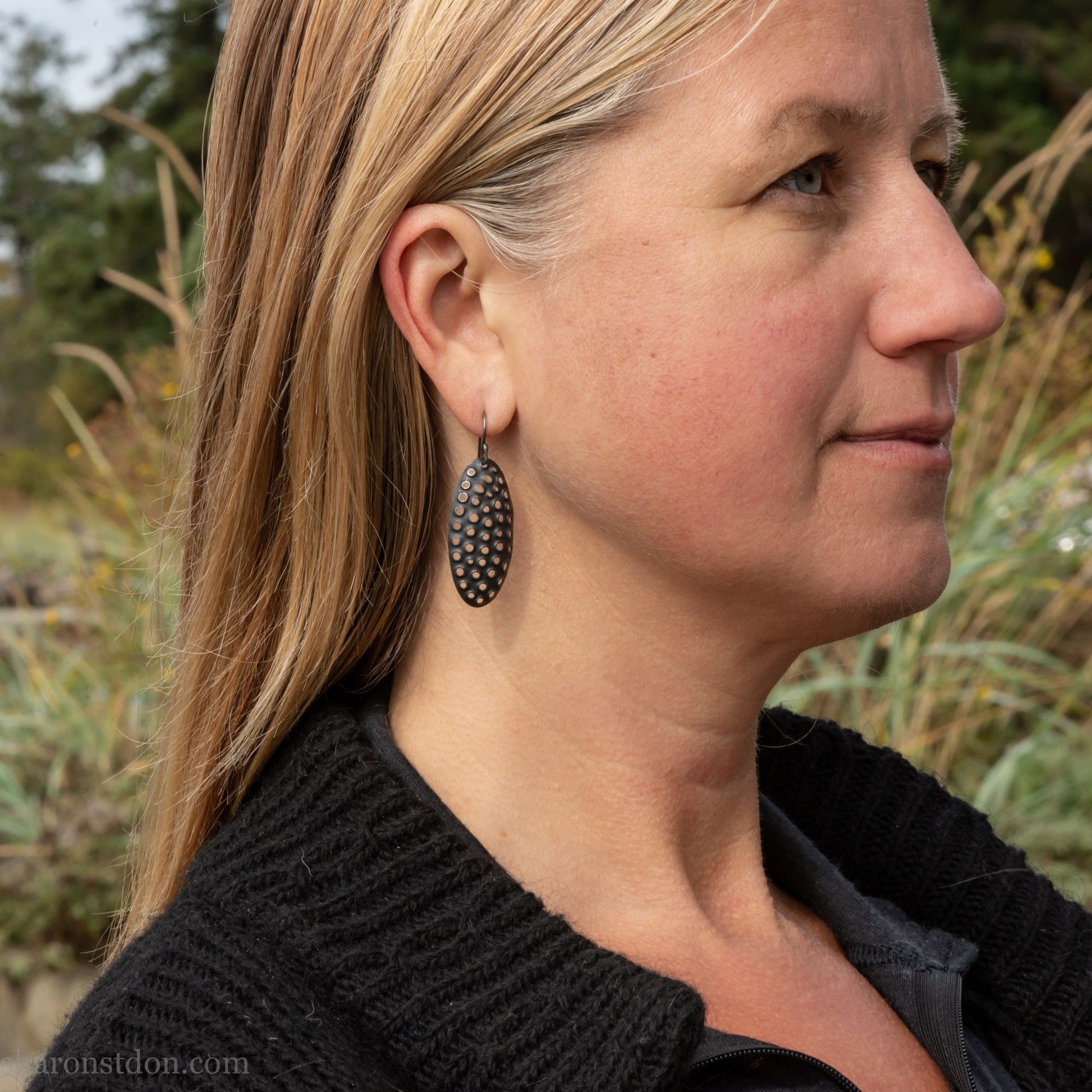 38mm solid 925 sterling silver oval disc earrings worn on ear, hand-punched pattern, flat matte black oxidized finish.