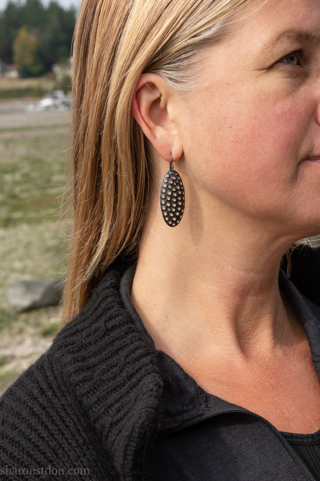 38mm solid 925 sterling silver oval disc earrings worn on ear, hand-punched pattern, flat matte black oxidized finish.