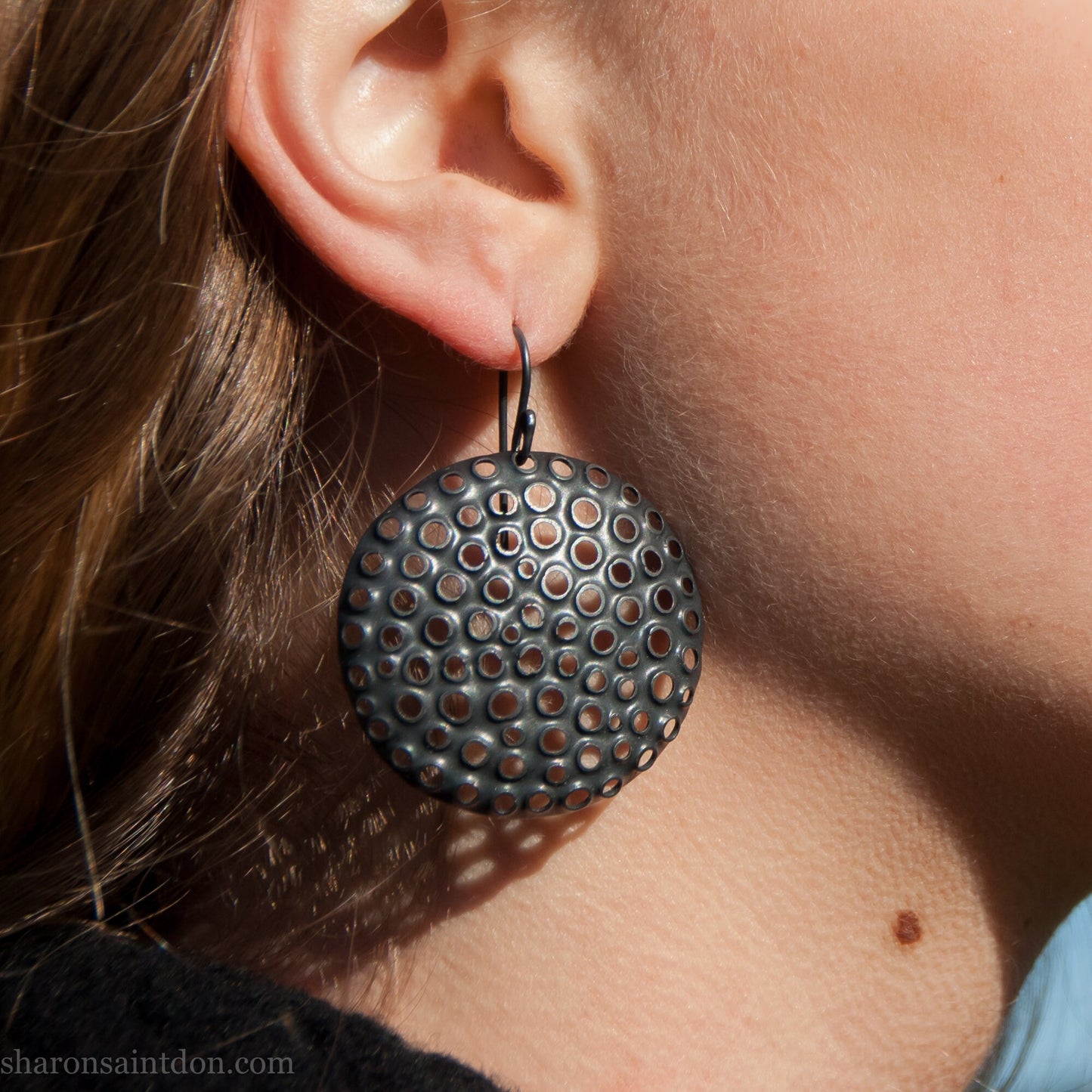 38mm solid 925 sterling silver sculptural round disc earrings worn on ear, hand-punched pattern, flat matte black oxidized finish.