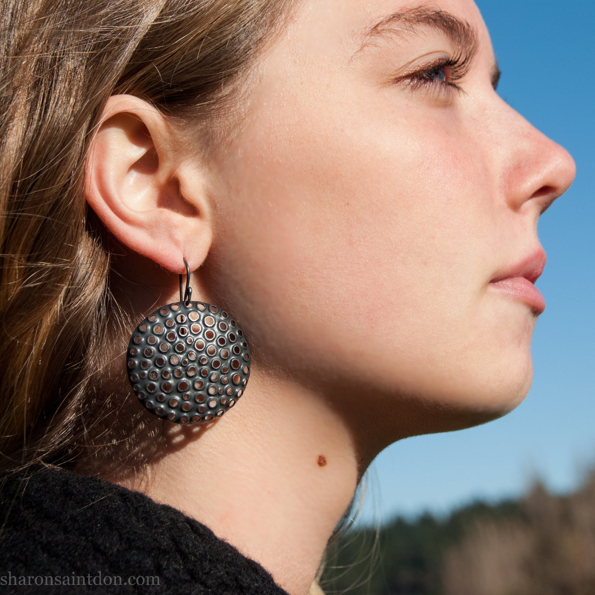 38mm solid 925 sterling silver sculptural round disc earrings worn on ear, hand-punched pattern, flat matte black oxidized finish.